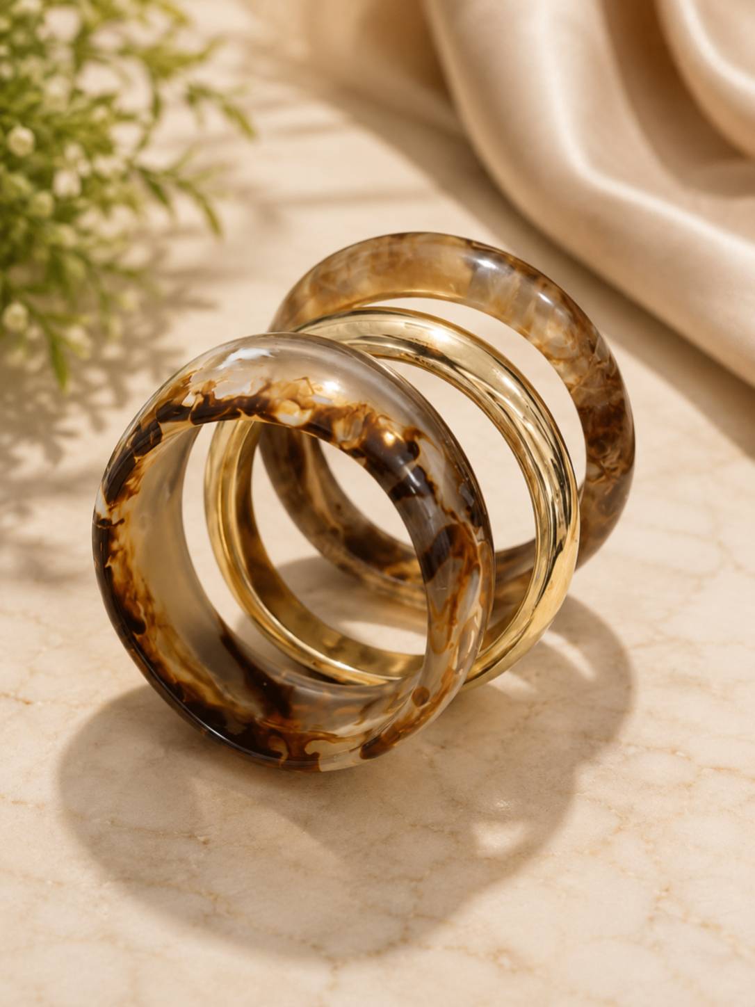 Three bangles — two brown marble resin and one gold-tone — leaning against each other on a marble surface