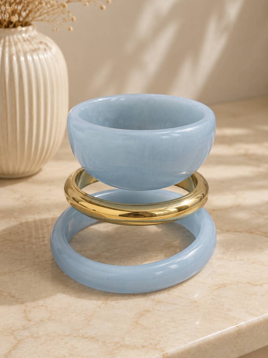 Three bangles displayed slightly separated on a marble surface, showing the individual shapes of each blue resin and gold-tone piece