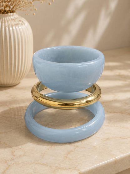 Three bangles displayed slightly separated on a marble surface, showing the individual shapes of each blue resin and gold-tone piece