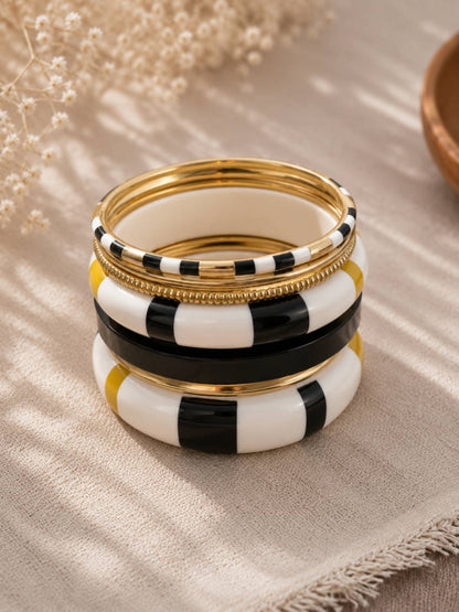 Stack of black white and gold-tone enamel bangles resting on a beige linen cloth with dried flowers
