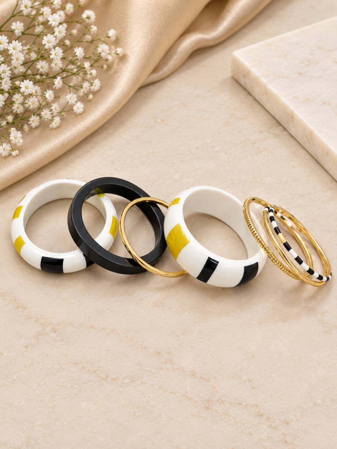 Five individual enamel and gold-tone bangles laid flat in a fan arrangement on a marble surface