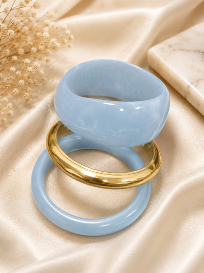 Blue marble resin bangles and gold-tone bangle laid flat separately on cream satin fabric with dried flowers