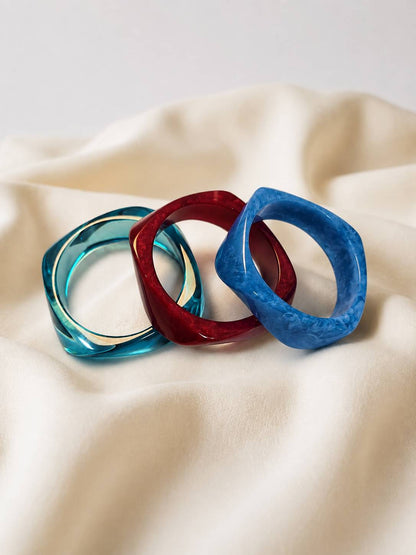 Cobalt blue, deep red and teal resin bangles arranged side by side on cream draped fabric