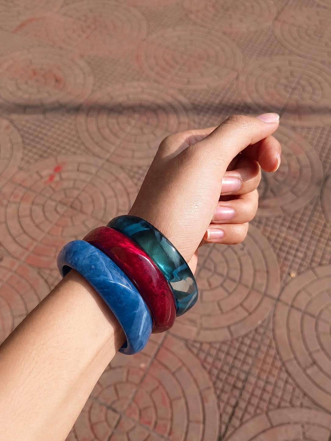 All three resin marble bangles worn together on a woman's wrist against a terracotta patterned background
