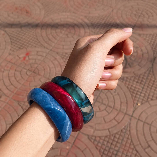 All three resin marble bangles worn together on a woman's wrist against a terracotta patterned background