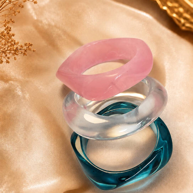 Three stacked resin bangles in pink, clear and teal on golden satin fabric with dried florals