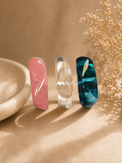 Pink, clear and teal resin bangles standing upright beside a stone bowl and dried flowers