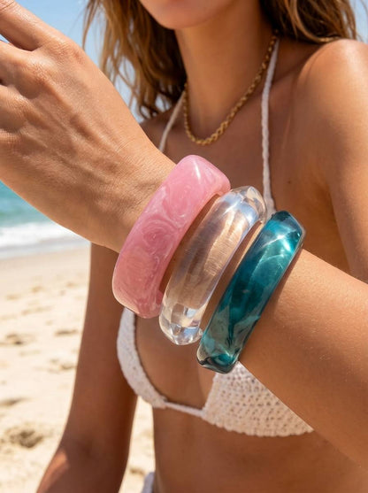 Model wearing all three stacked resin bangles on her wrist at the beach in sunlight