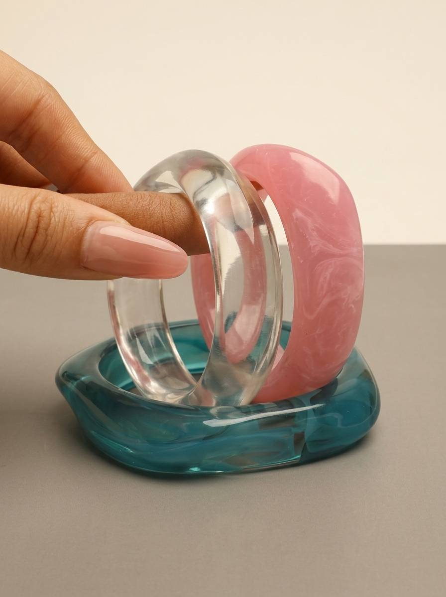 Close-up of stacked pink, clear and teal resin bangles on model's wrist at a sunny beach