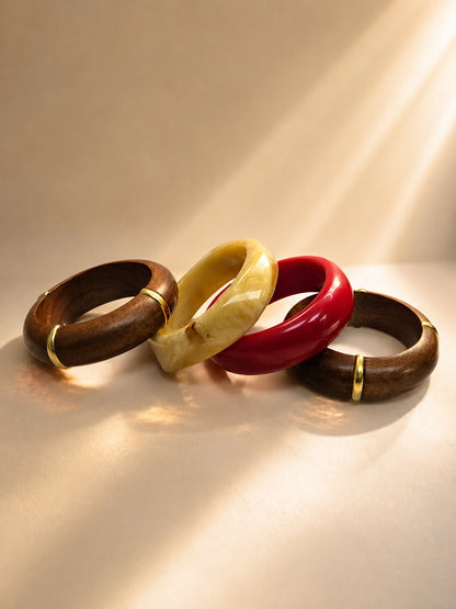 Four bangles laid flat in sunlight — two wood with gold accents, one cream marble resin, one red glossy resin