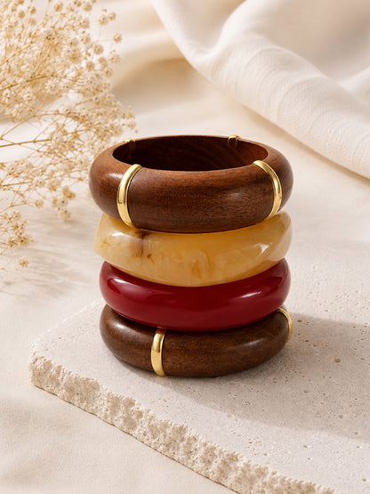 Four bangles stacked vertically on a stone surface beside dried flowers and white fabric