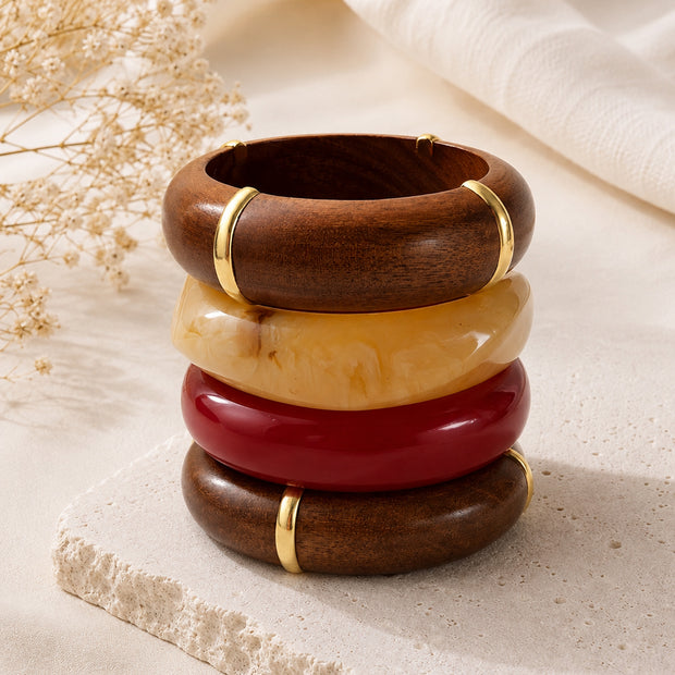 Four bangles stacked vertically on a stone surface beside dried flowers and white fabric