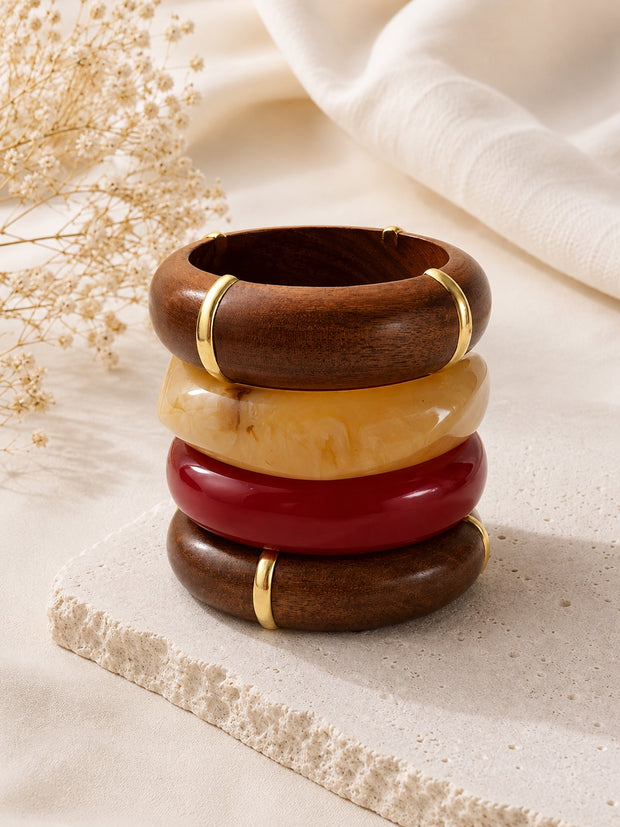 Four bangles stacked vertically on a stone surface beside dried flowers and white fabric