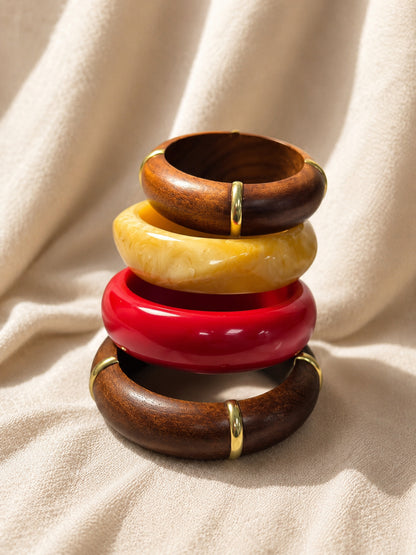 Four bangles stacked in a tower against a draped cream linen background showing wood grain and resin detail