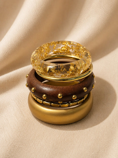 Four stacked bangles piled vertically showing resin with gold foil on top, studded wood bangle in the middle, and matte gold cuff at the base
