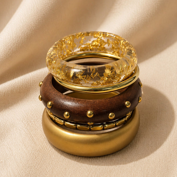 Four stacked bangles piled vertically showing resin with gold foil on top, studded wood bangle in the middle, and matte gold cuff at the base