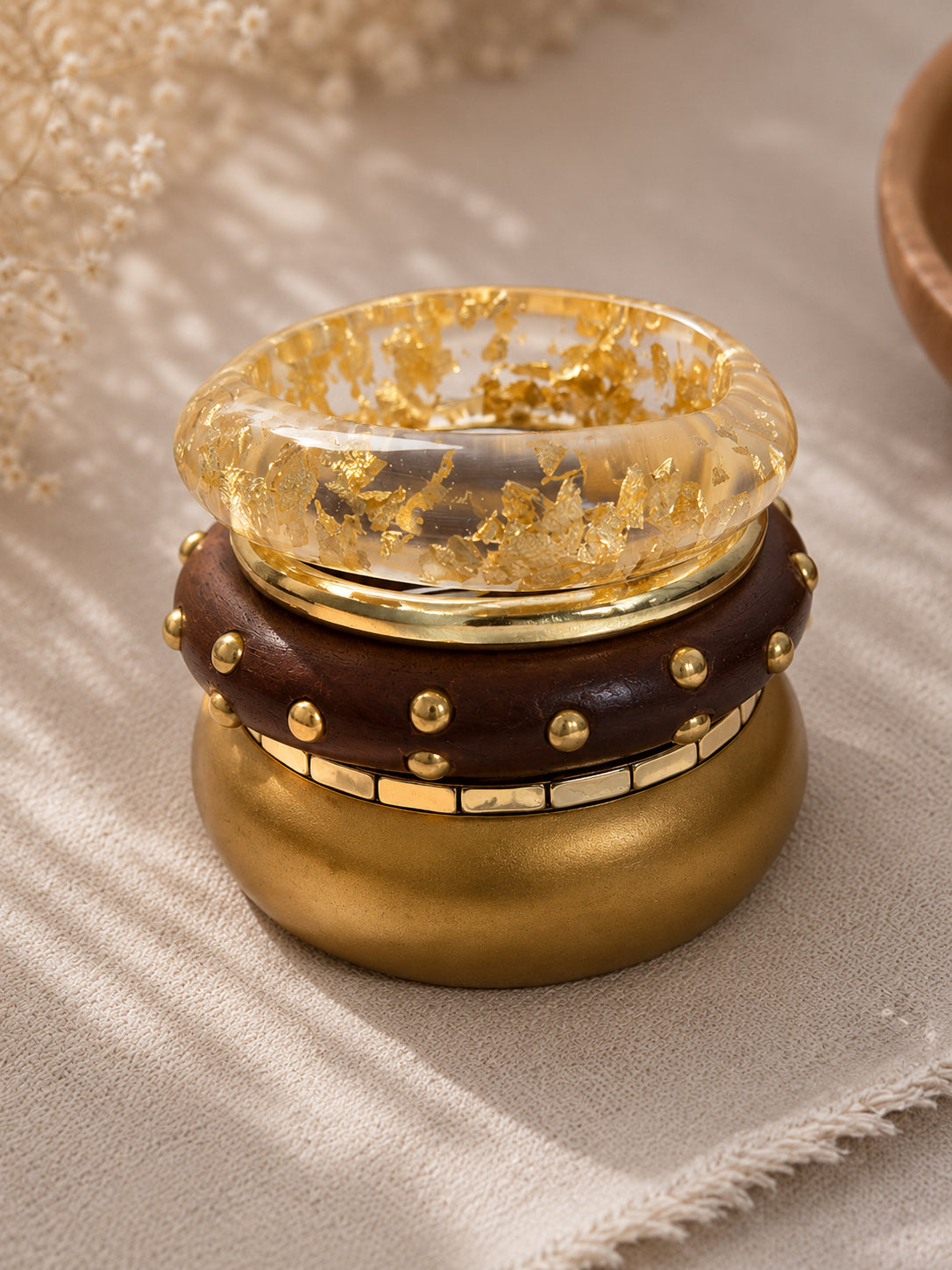 Side angle of the four bangles stacked together on a linen surface with dried flowers in the background