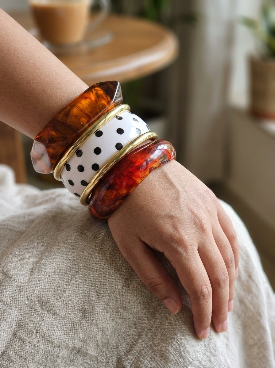 Stacked tortoiseshell resin bangles with polka-dot and gold-tone rings worn on a woman's wrist resting on her knee