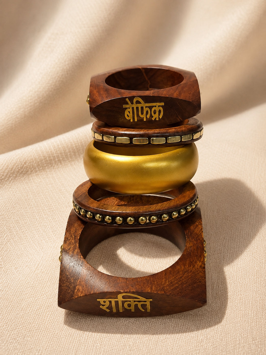 Side view of all five bangles stacked vertically showing the Befikr wood bangle, tile-inlay band, gold dome bangle, bead-trim band and Shakti wood bangle