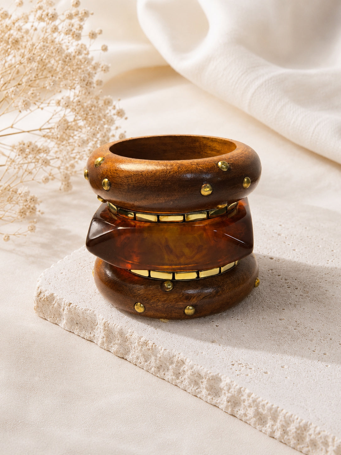 All three bangles stacked upright on a stone tile with dried flowers, showing the layered profile of wood and resin