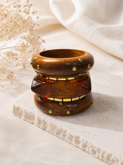 All three bangles stacked upright on a stone tile with dried flowers, showing the layered profile of wood and resin