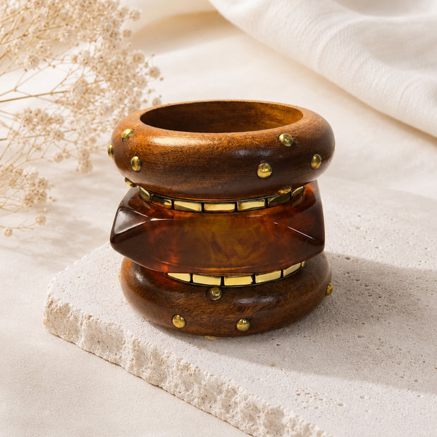 All three bangles stacked upright on a stone tile with dried flowers, showing the layered profile of wood and resin