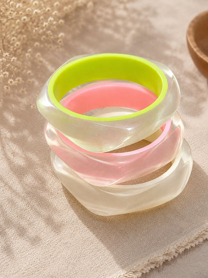 Stack of four iridescent resin bangles with neon green and pink accents on a linen cloth