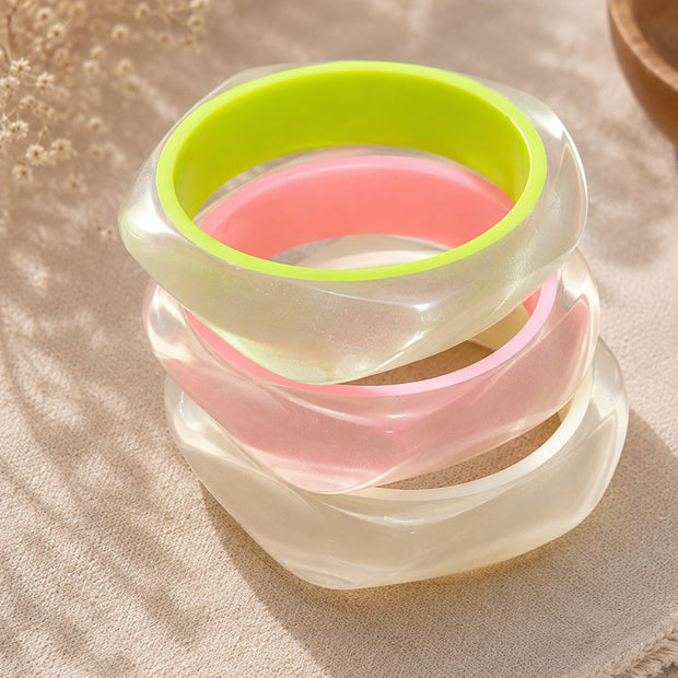 Stack of four iridescent resin bangles with neon green and pink accents on a linen cloth