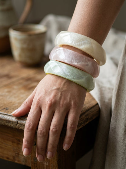 Woman wearing three stacked pearlescent resin bangles in ivory, pink, and mint on her wrist