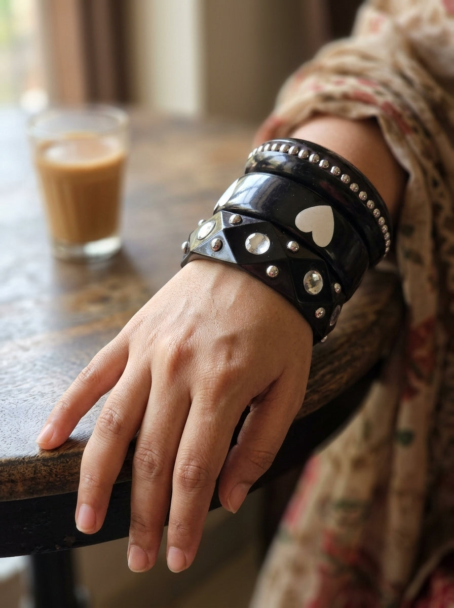 All three black resin bangles stacked and worn together on a woman's wrist resting on a wooden table