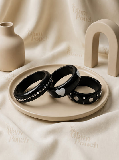 Three black resin bangles displayed flat on a beige ceramic tray with The Glam Pouch branded cloth background