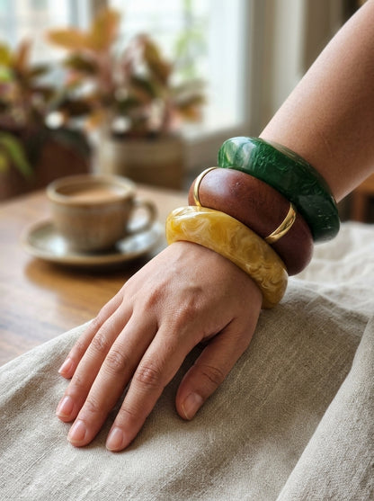 Three resin and wood bangles stacked on a woman's wrist resting on linen cloth with a coffee cup in the background