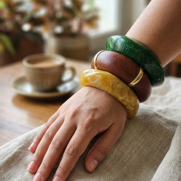 Three resin and wood bangles stacked on a woman's wrist resting on linen cloth with a coffee cup in the background