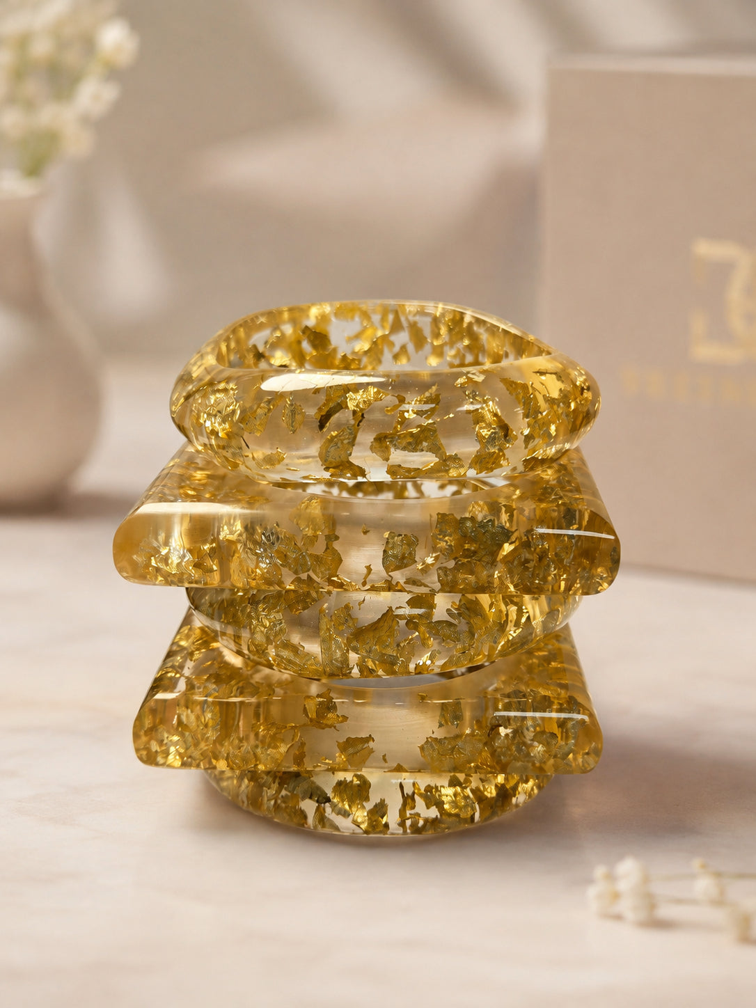 Three clear resin bangles with suspended gold foil stacked in a neat tower on a light marble surface