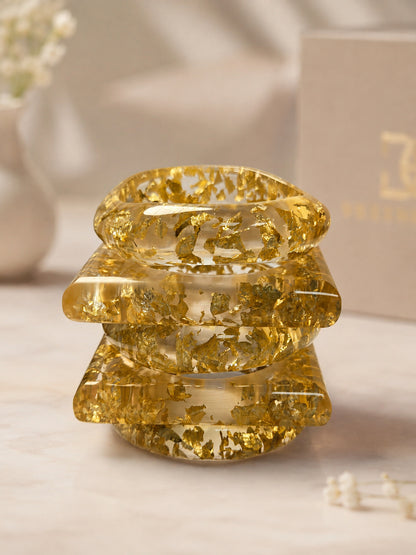 Three clear resin bangles with suspended gold foil stacked in a neat tower on a light marble surface