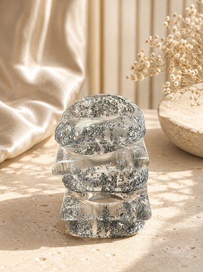 Stack of four chunky clear resin bangles with silver leaf embedded, standing on a textured stone surface