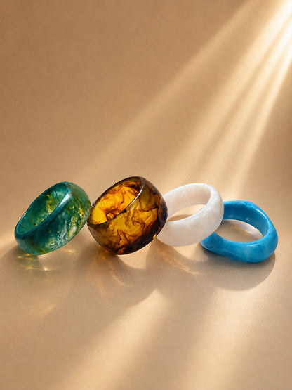 Four marble resin bangles in teal, amber, white and blue laid flat on a warm beige surface in sunlight