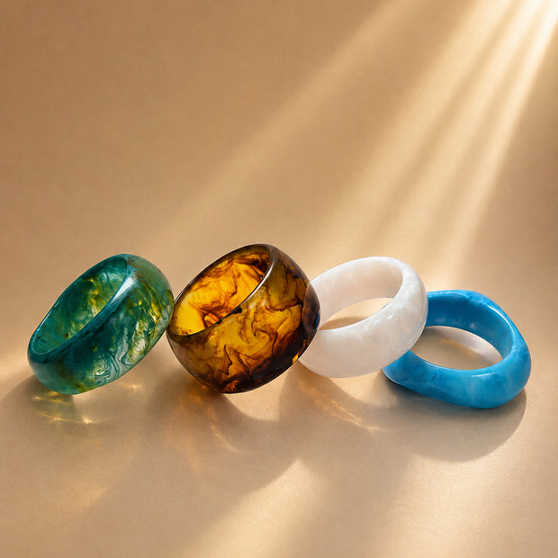 Four marble resin bangles in teal, amber, white and blue laid flat on a warm beige surface in sunlight