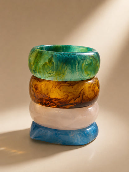Four resin marble bangles stacked vertically showing teal green on top, then amber, white and blue at base