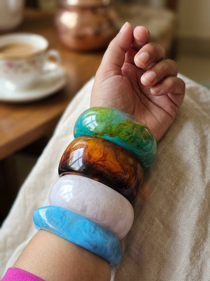 All four marble resin bangles worn stacked on a woman's wrist resting on a white cloth