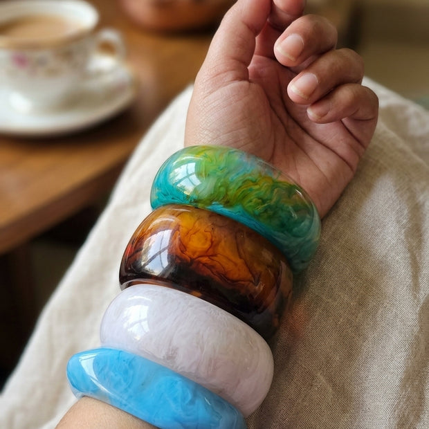 All four marble resin bangles worn stacked on a woman's wrist resting on a white cloth