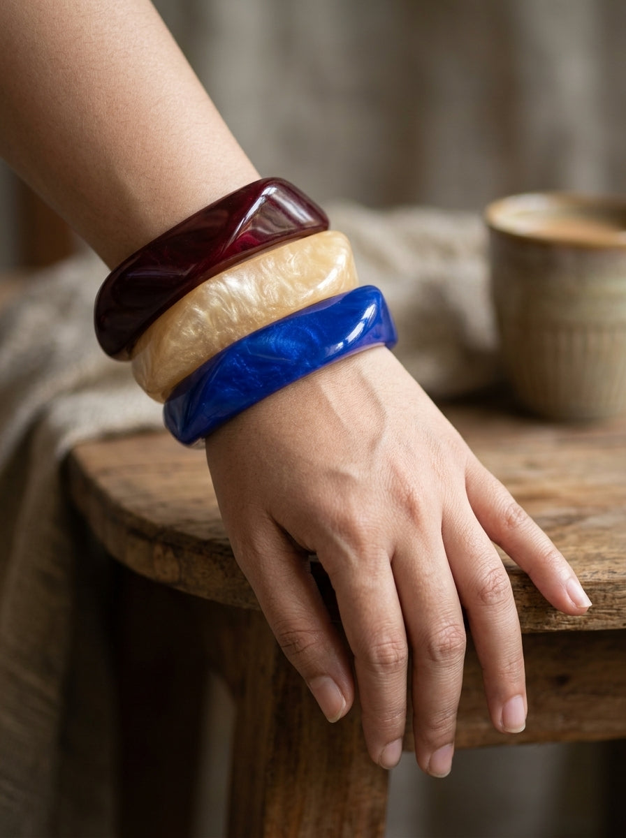 All three resin bangles stacked on a woman's wrist resting on a wooden stool