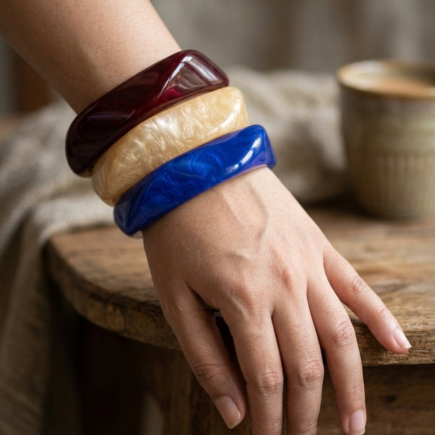 All three resin bangles stacked on a woman's wrist resting on a wooden stool