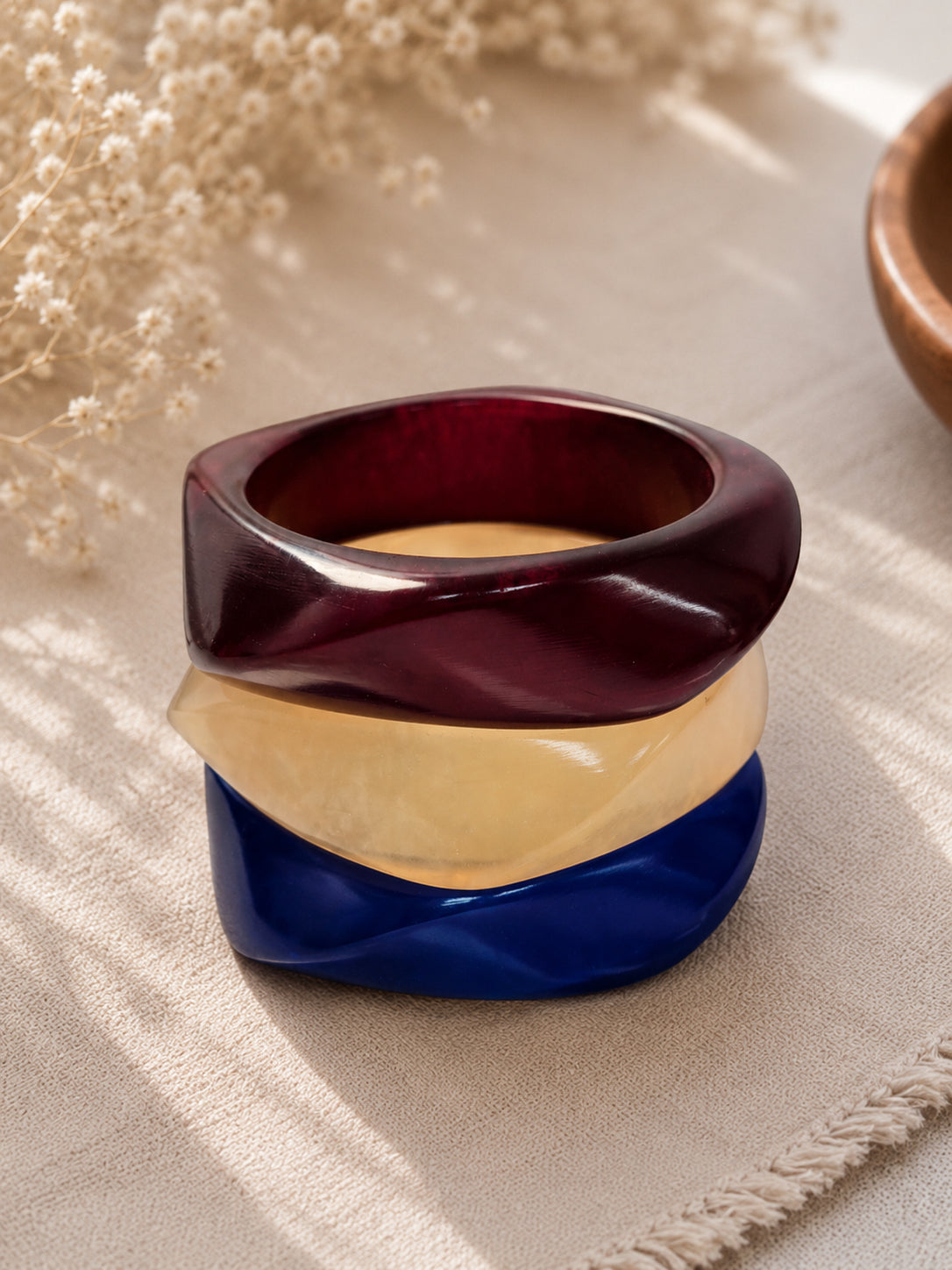 Close-up of stacked burgundy, ivory and cobalt blue resin bangles showing faceted twisted surface
