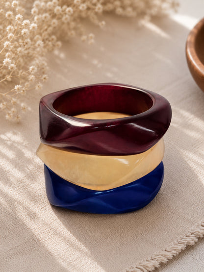 Close-up of stacked burgundy, ivory and cobalt blue resin bangles showing faceted twisted surface
