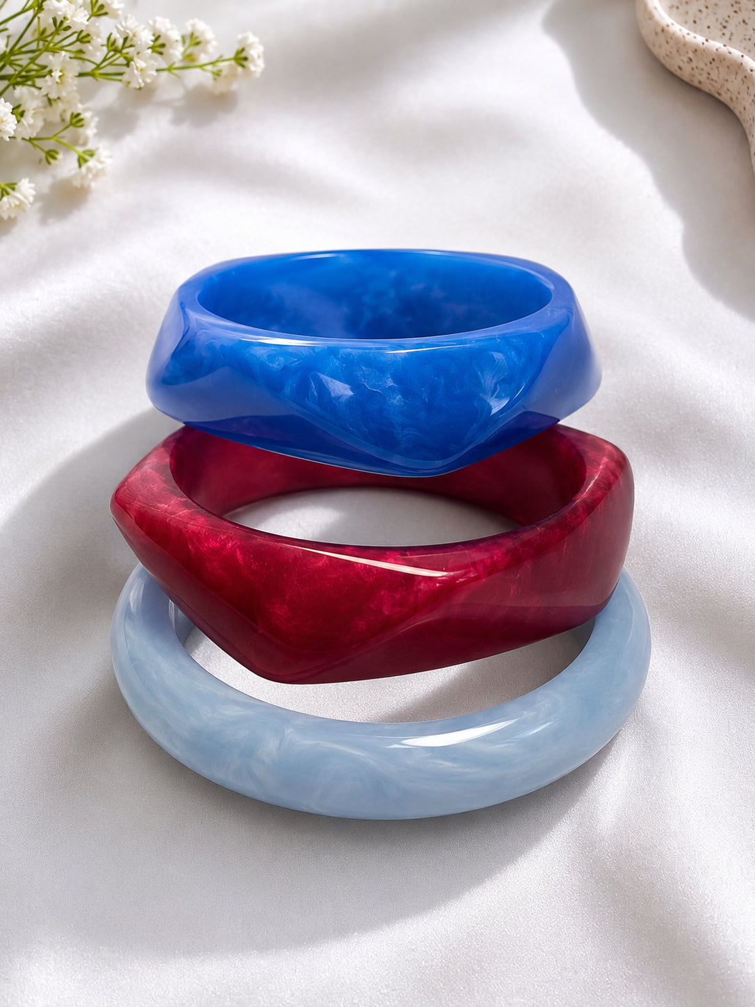 Three marble resin bangles stacked neatly on white fabric showing blue on top, burgundy in the middle, and powder blue at the base