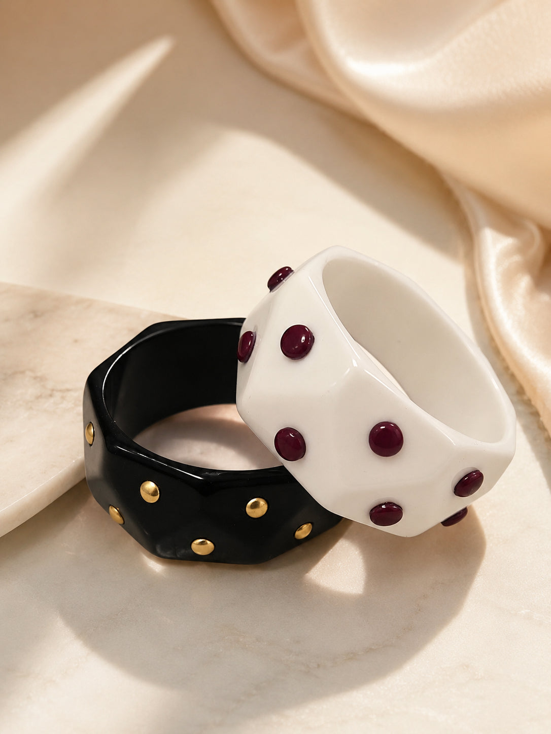 Black and white faceted resin cuff bangles with gold and burgundy studs on marble surface