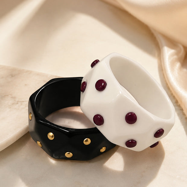Black and white faceted resin cuff bangles with gold and burgundy studs on marble surface