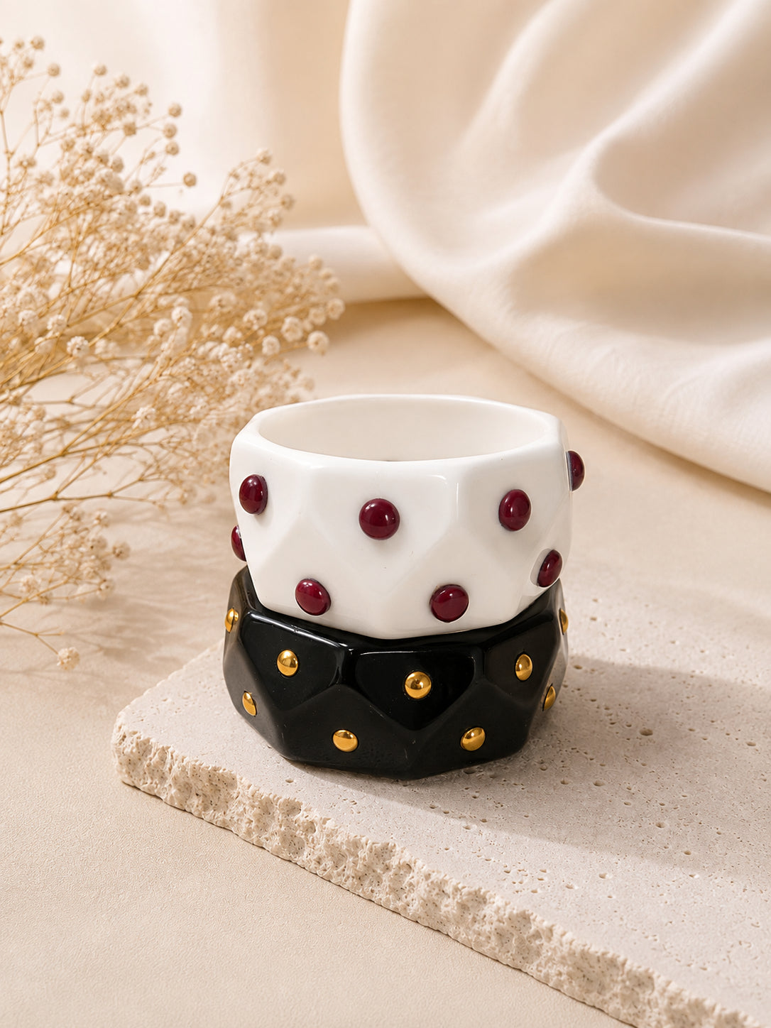 White resin cuff with burgundy studs stacked on black resin cuff with gold studs on stone platform