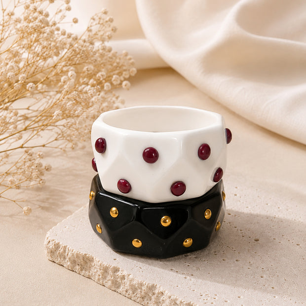 White resin cuff with burgundy studs stacked on black resin cuff with gold studs on stone platform